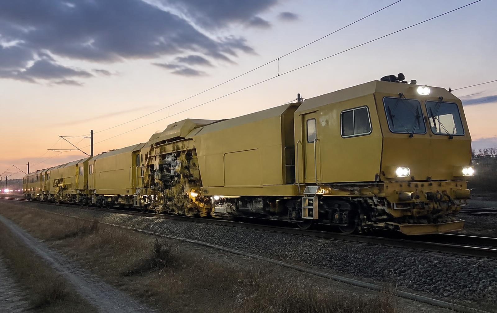 Unbranded ballast cleaning consist and track recording machine on a rail line at dusk